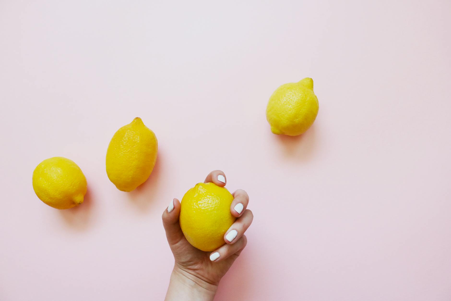 Une main tenant un citron frais sur un fond rose pastel