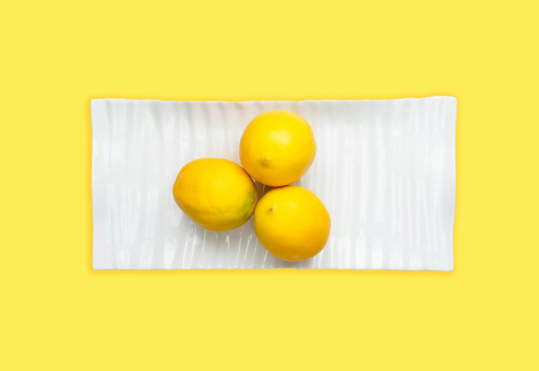 Trois citrons frais disposés sur une assiette blanche avec un fond jaune vibrant, soulignant la fraîcheur et l'énergie
