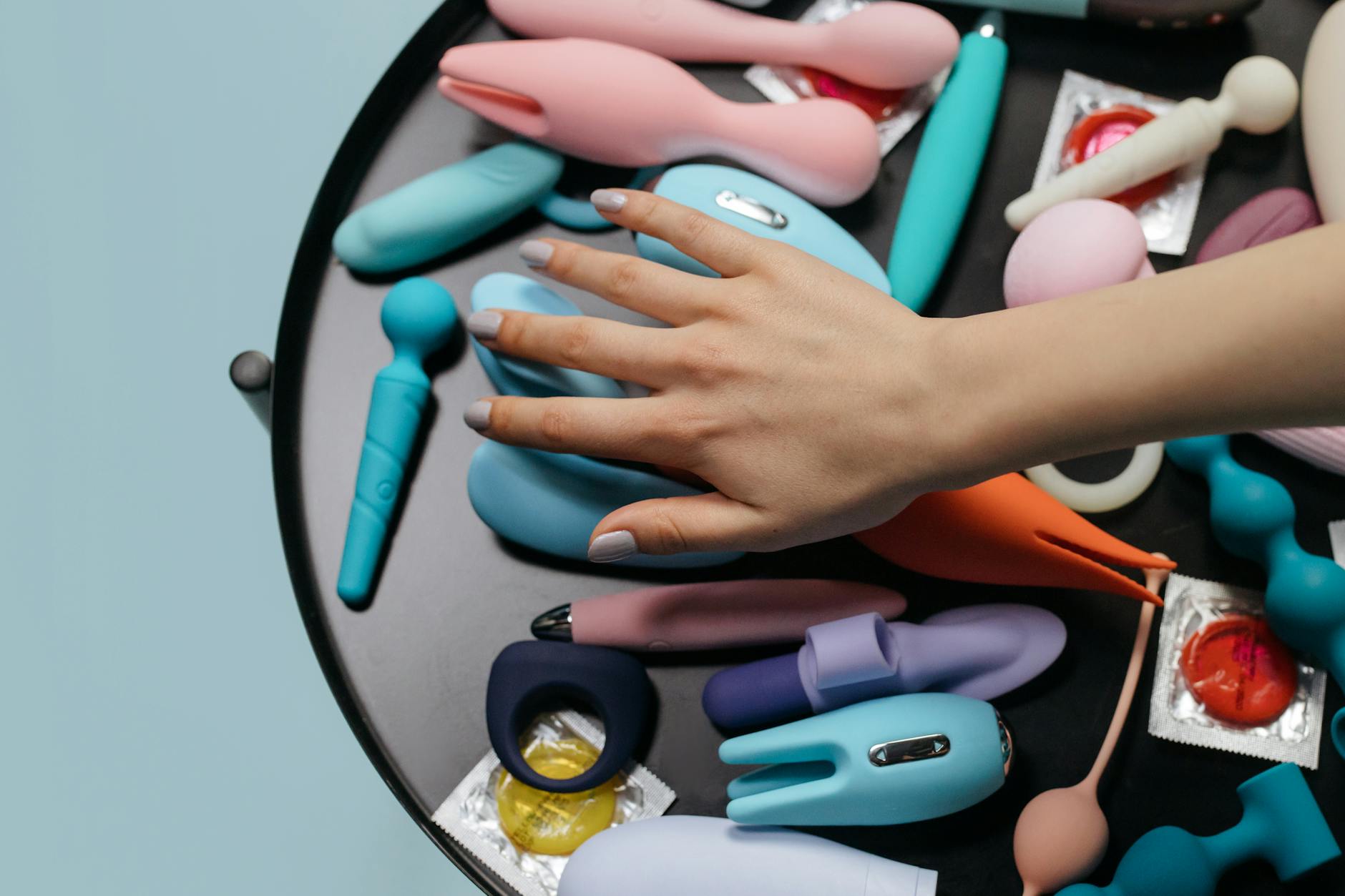 Deux mains tenant des vibrateurs rose et bleu en silicone sur fond pastel
