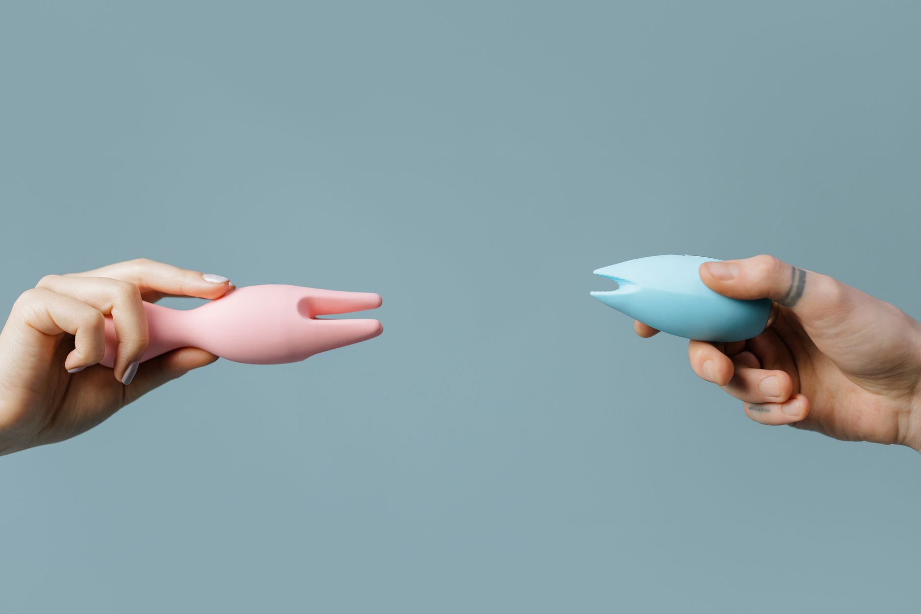 Photo de mains tenant des vibrateurs rose et bleu contre un fond pastel.