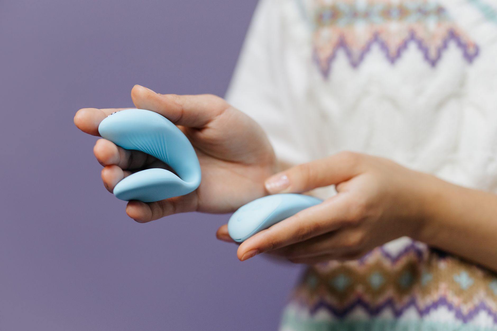 Gros plan sur les mains tenant un vibrateur bleu brillant Lem contre un fond violet.