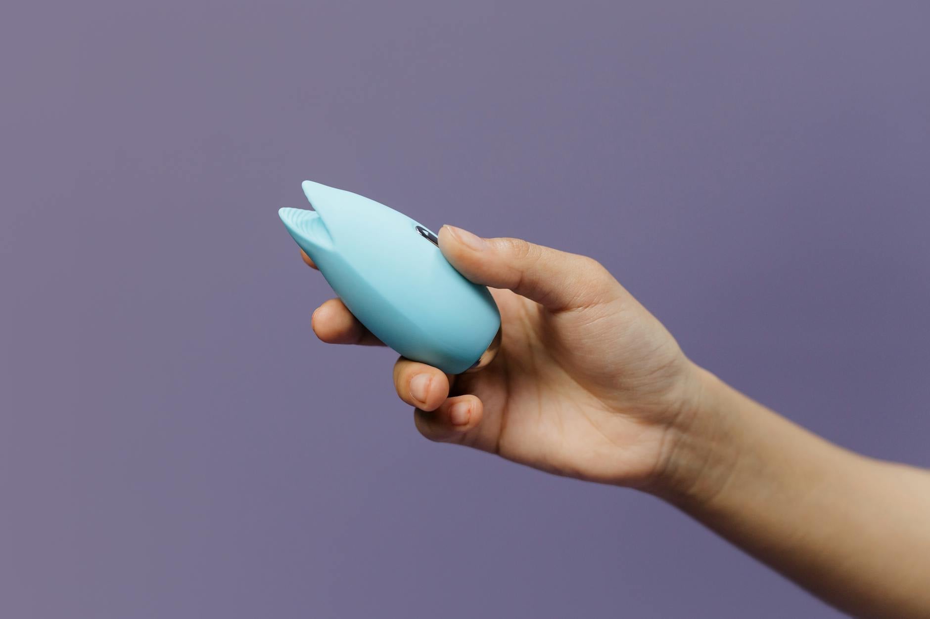 Deux mains tenant des vibrateurs rose et bleu sur fond pastel