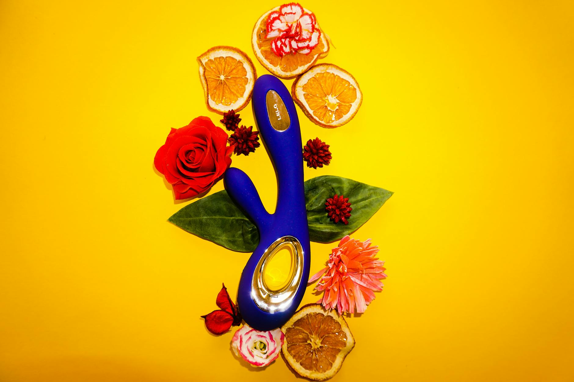 Vibrateur citron Lem entouré de fleurs et tranches d'orange sur fond jaune